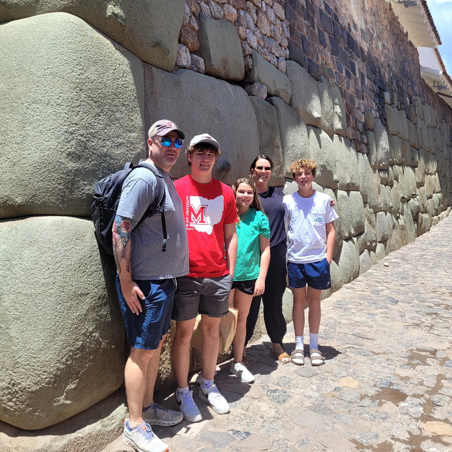 Família durante visita às ruas históricas de Cusco, junto a um muro de pedras incas