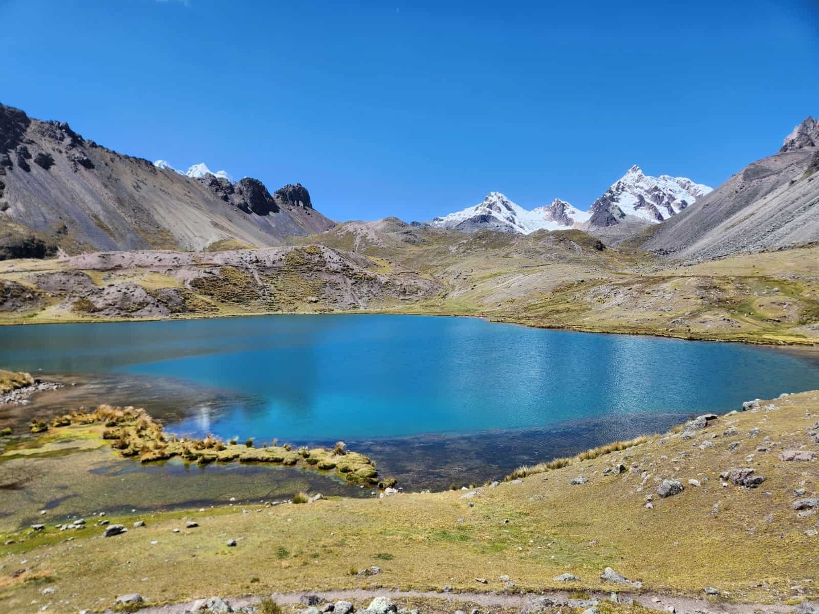 Lago azul das Sete Lagoas de Ausangate, com margens andinas e picos nevados ao fundo