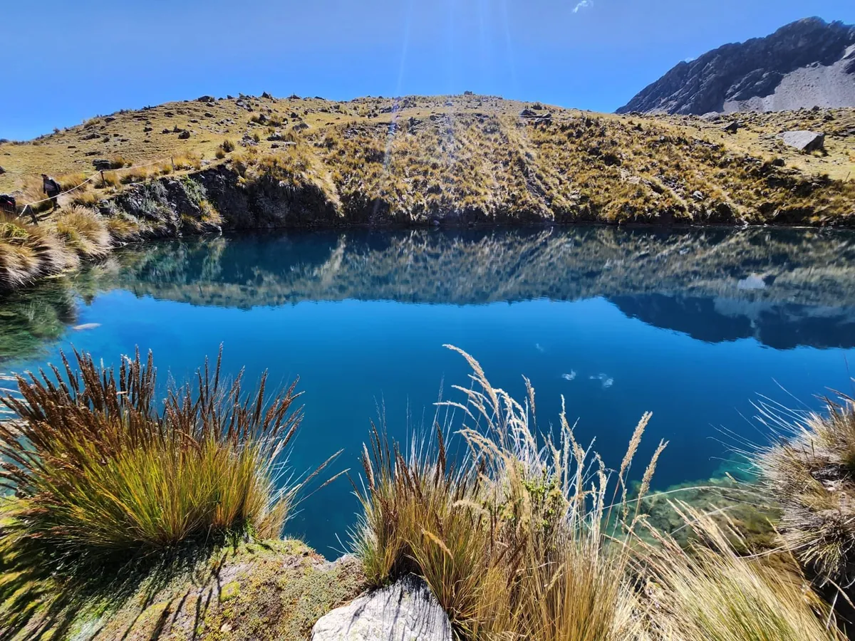 Lagoa no circuito de Ausangate, entre montanhas e vegetação dos Andes.