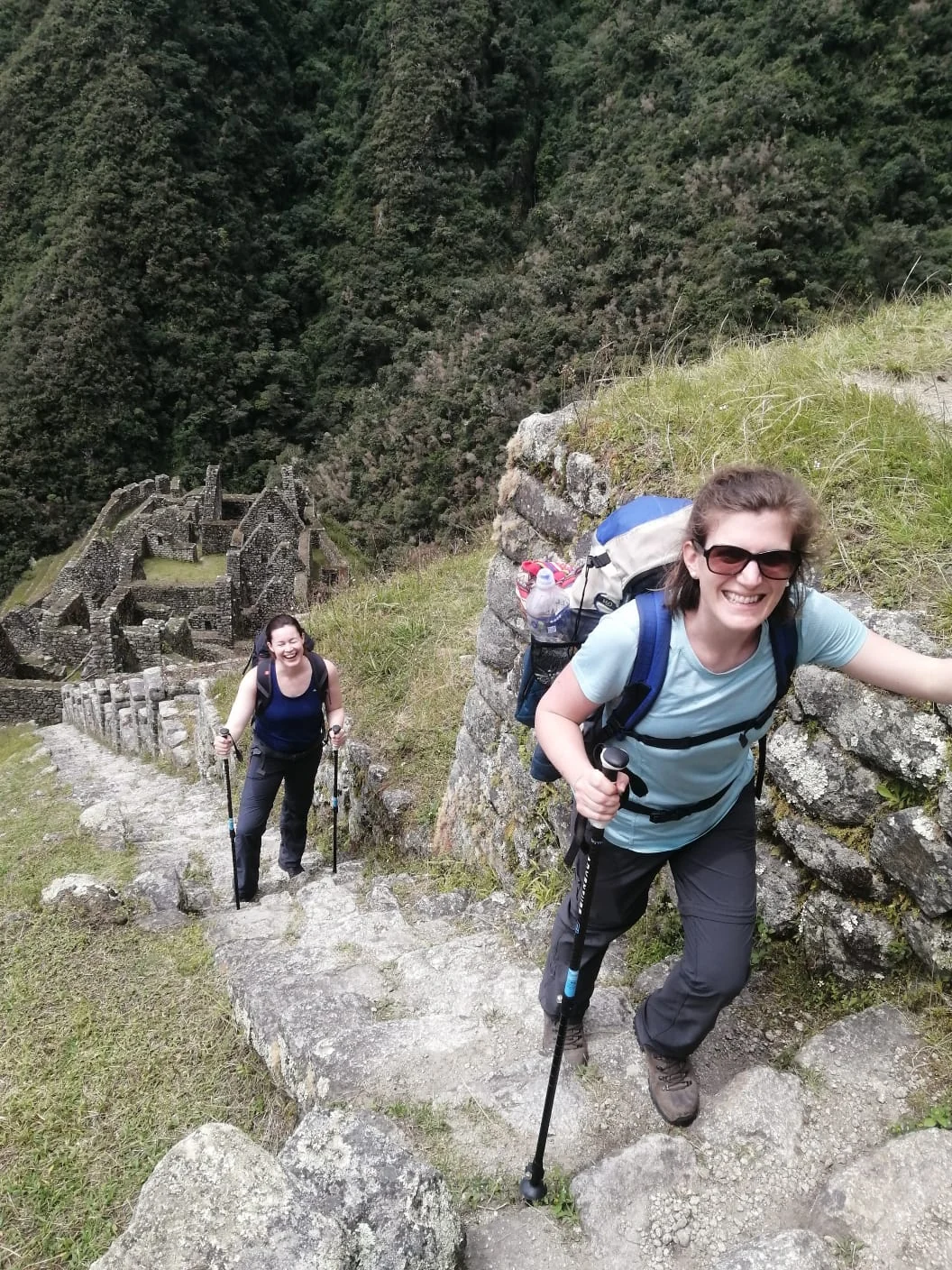 Viajantes com mochilas e bastões subindo uma escadaria de pedra na Trilha Inca